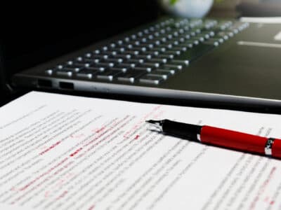 Proofreading sheet on table with red pen and laptop