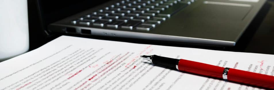Proofreading sheet on table with red pen and laptop